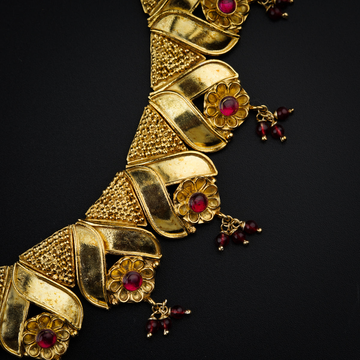 a gold necklace with red stones on a black surface