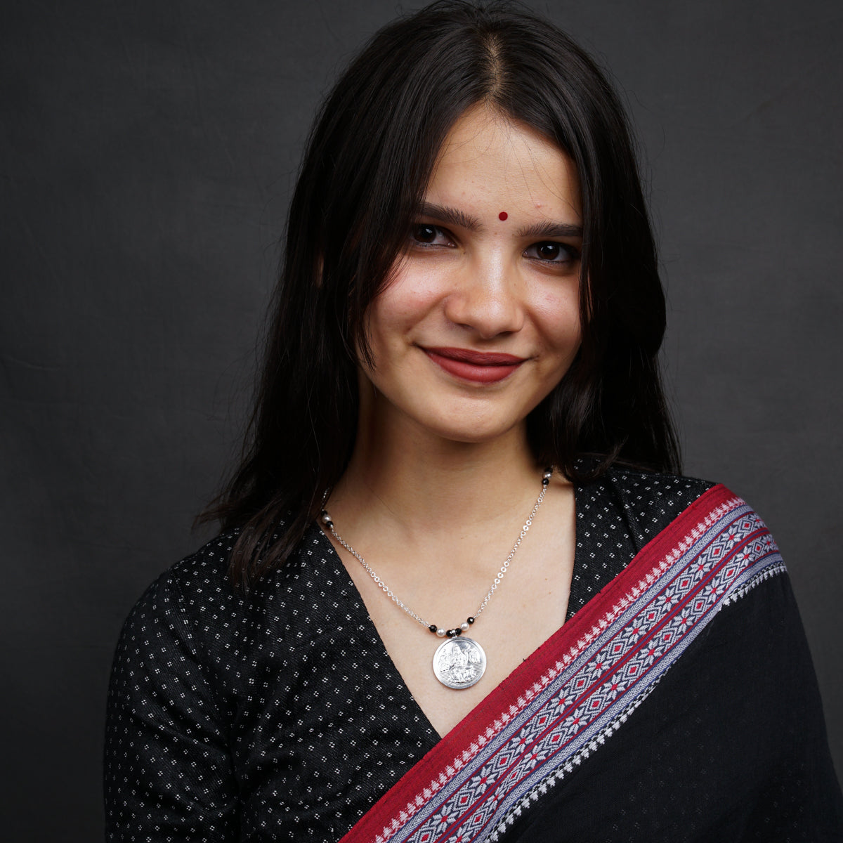 a woman in a black and red sari smiles at the camera