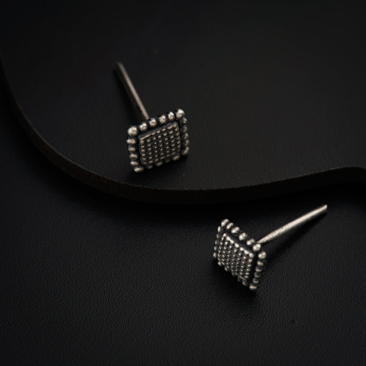 a pair of silver studded earrings sitting on top of a black surface