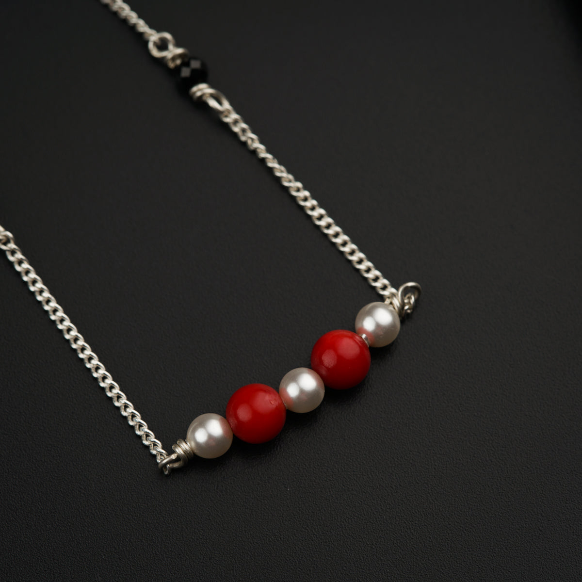 a necklace with three pearls and a red bead