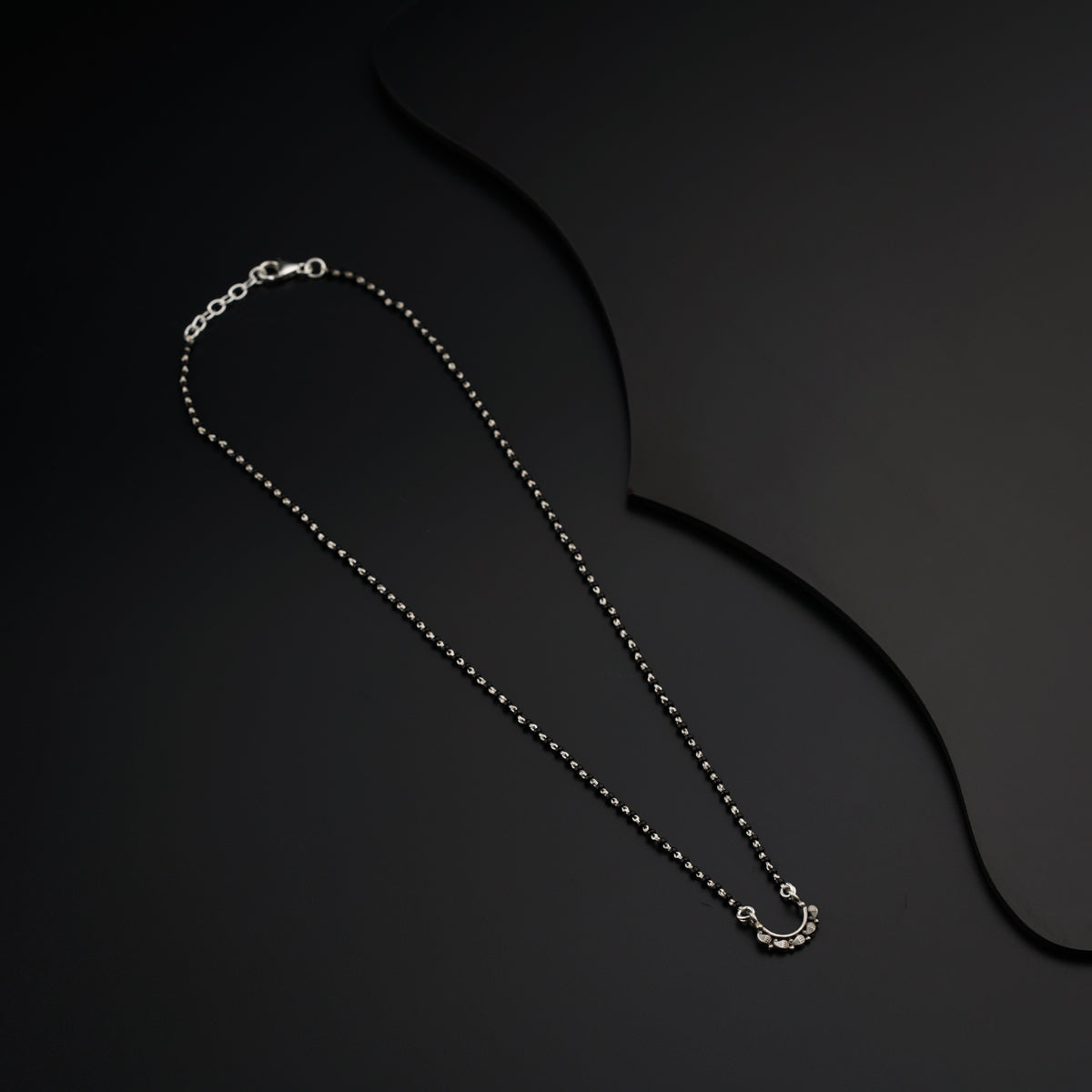 a silver necklace with a chain on a black background