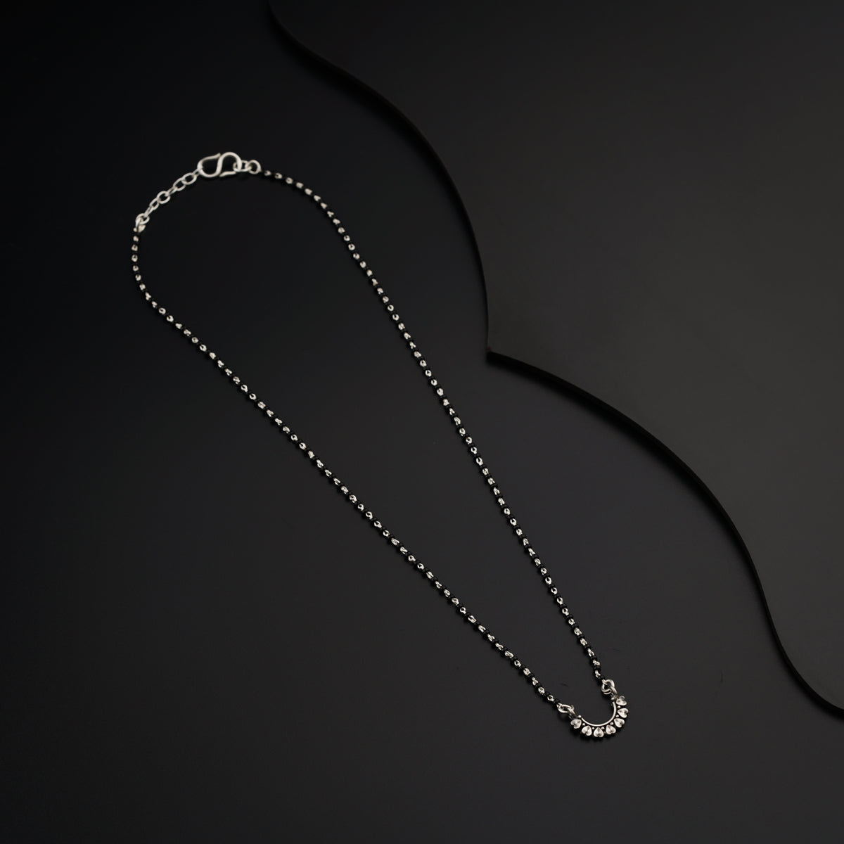 a silver necklace with a chain on a black background
