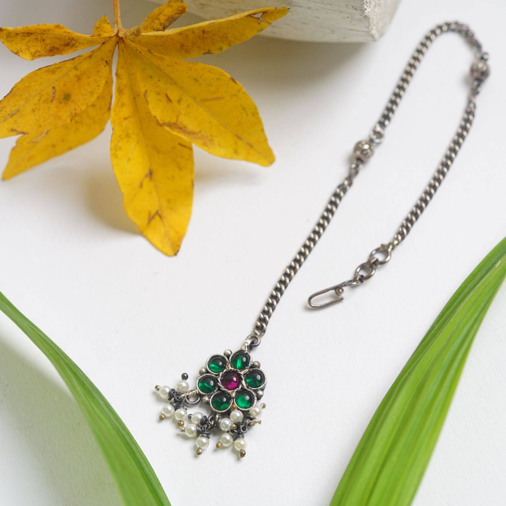 a green and white necklace sitting on top of a green leaf