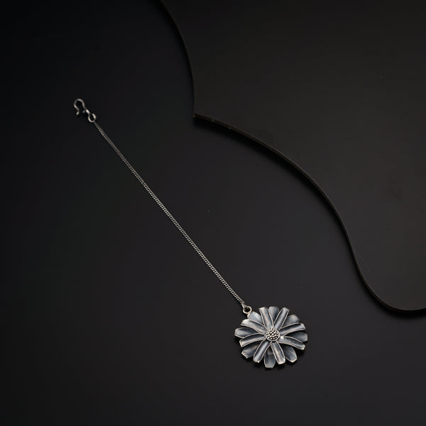 a silver necklace with a flower on a black background