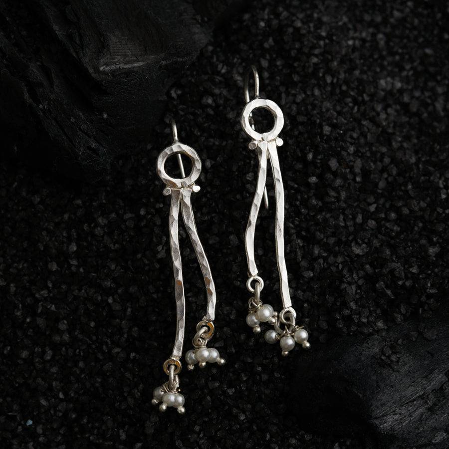 a pair of silver earrings with pearls hanging from them