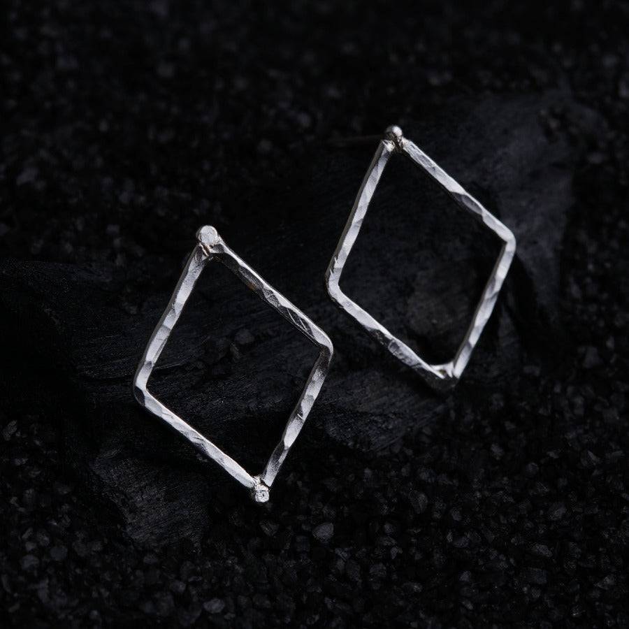 a pair of silver square earrings on a black surface