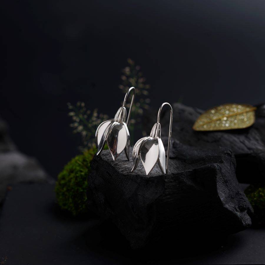 a pair of silver earrings sitting on top of a rock