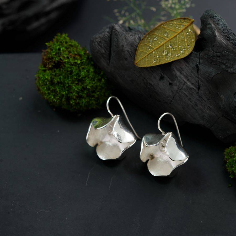 a pair of silver earrings sitting on top of a piece of wood