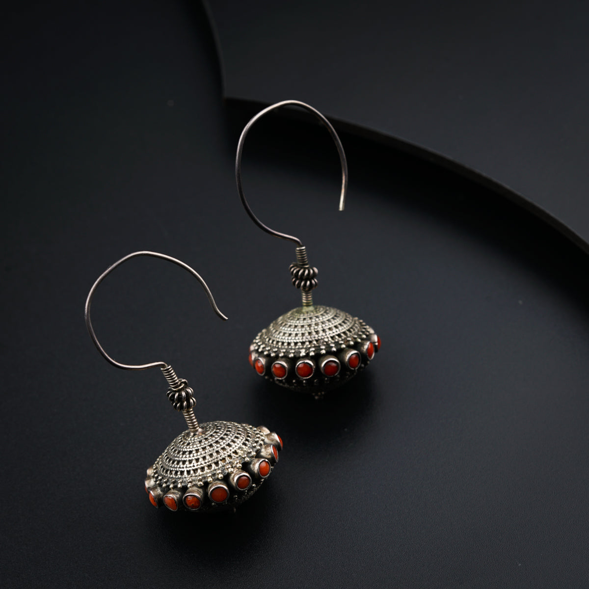 a pair of silver and red earrings on a black surface