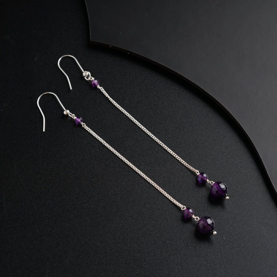 a pair of purple beads hanging from a pair of silver chain earrings