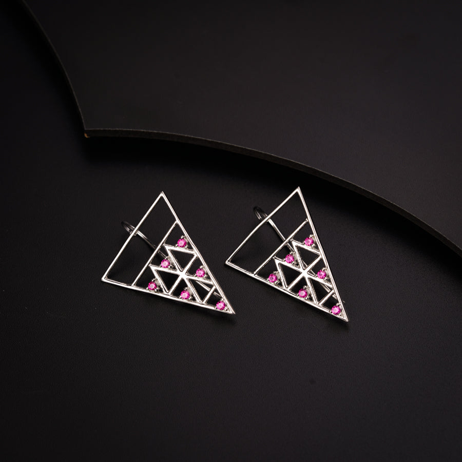 a pair of triangle shaped earrings with pink stones