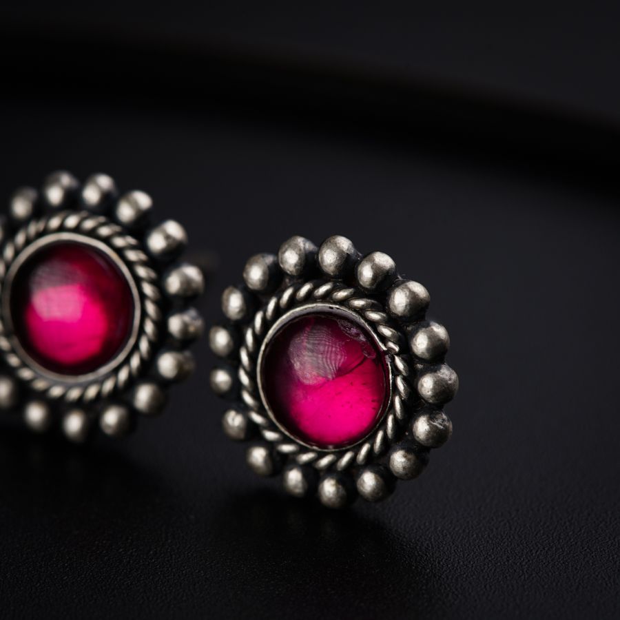 a pair of silver and pink earrings on a black surface