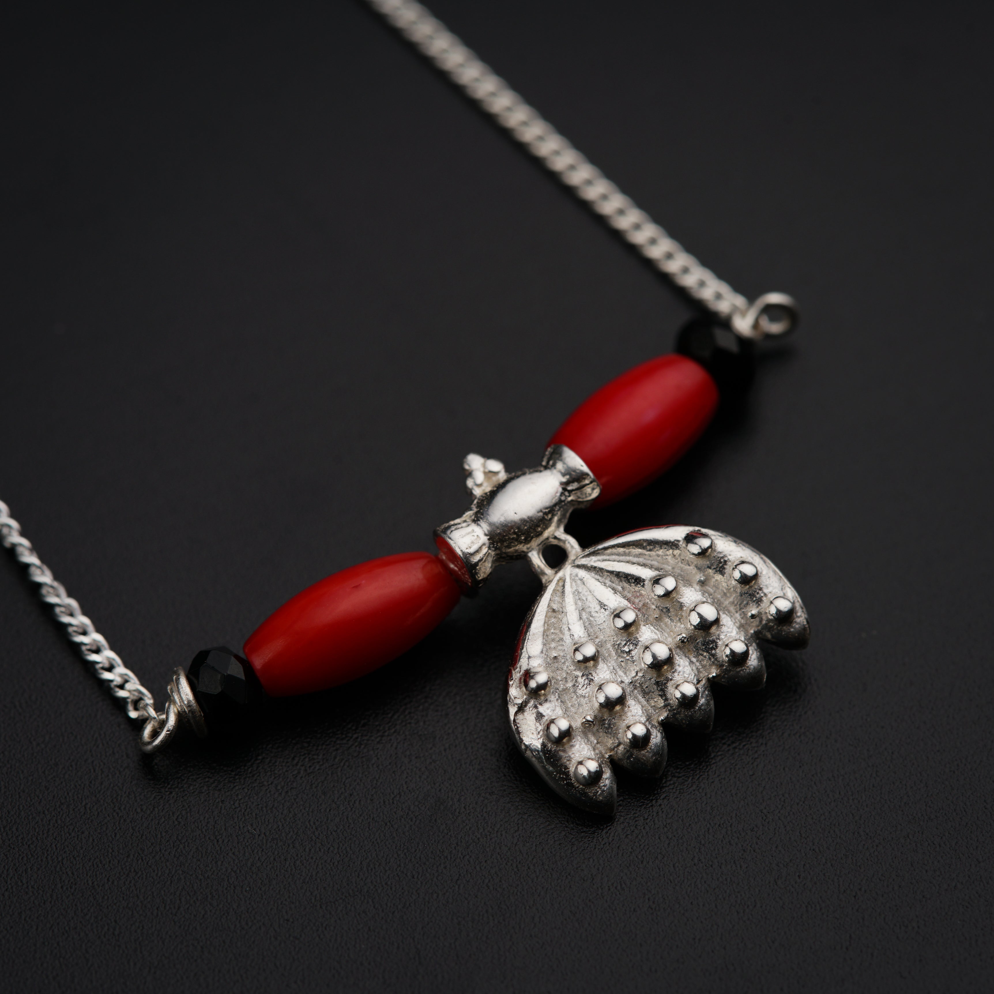a necklace with a red bead and a silver pendant