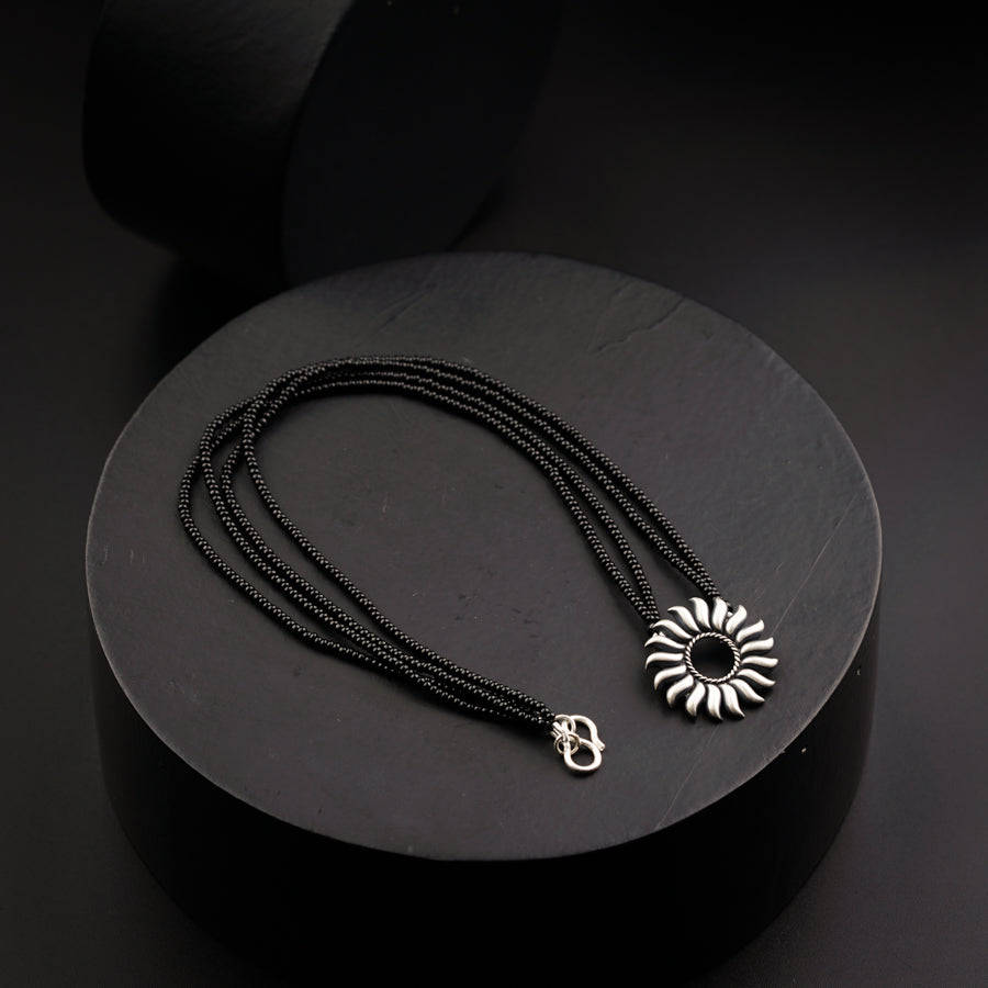 a black necklace with a silver pendant on it