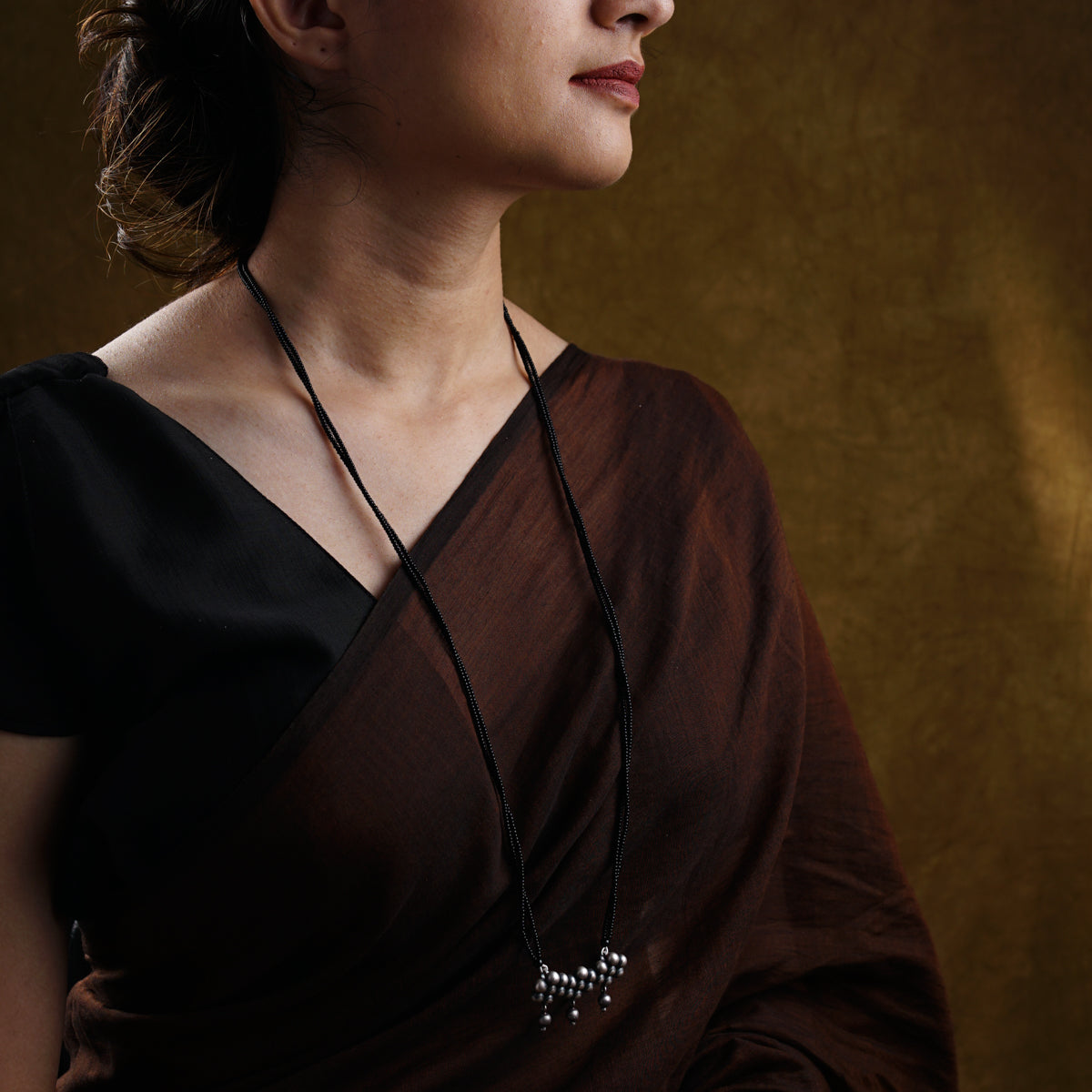 a woman wearing a brown dress and a black necklace