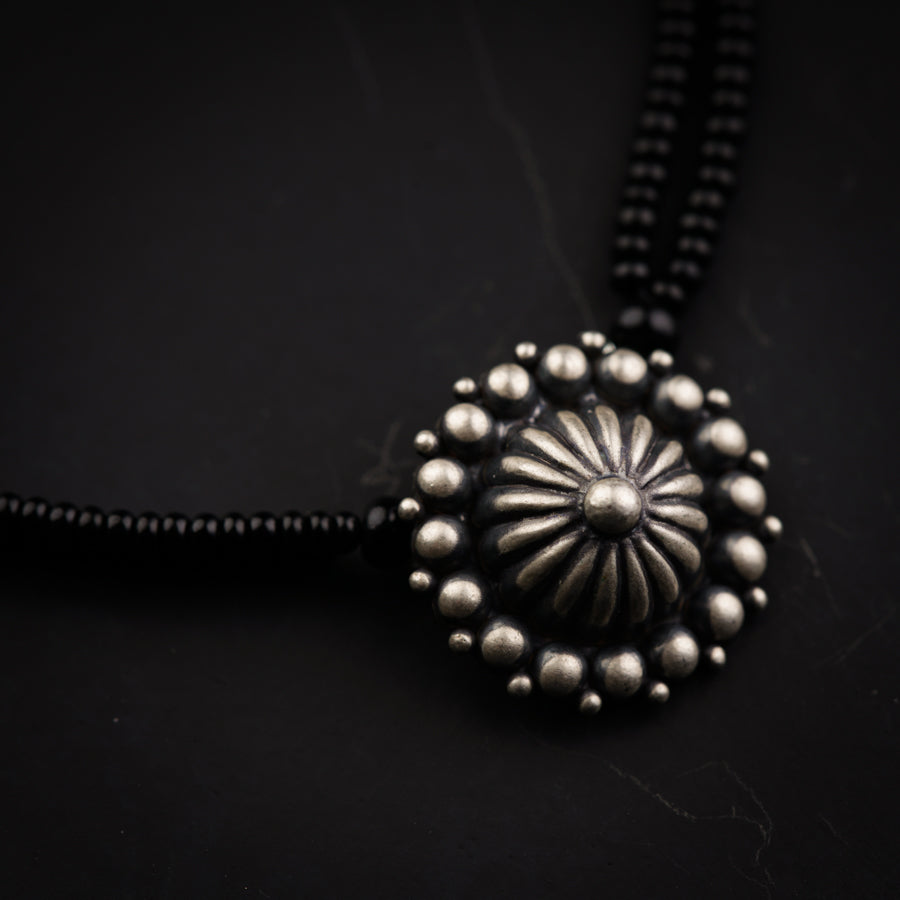 a black necklace with a silver flower on it
