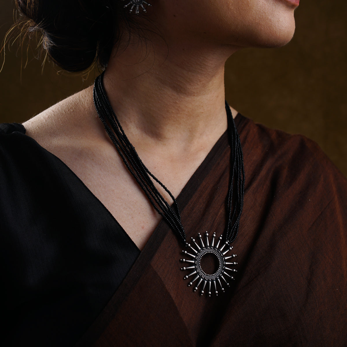 a woman wearing a black necklace and a brown shirt