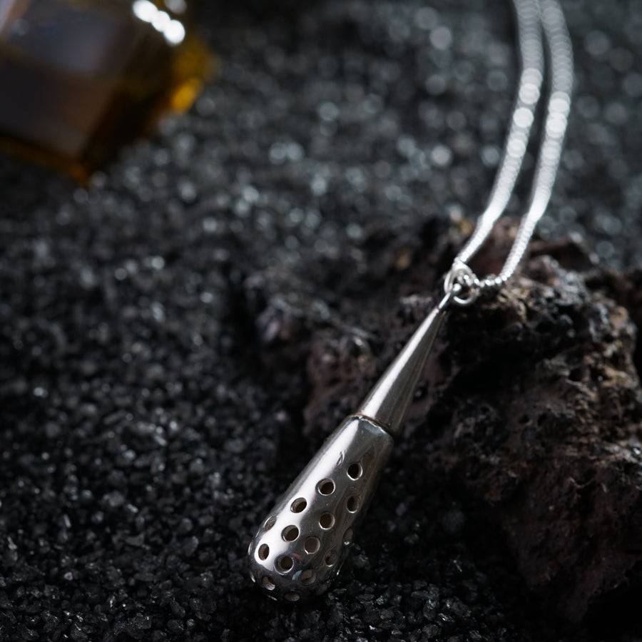 a necklace with a bottle of essential oils on a rock