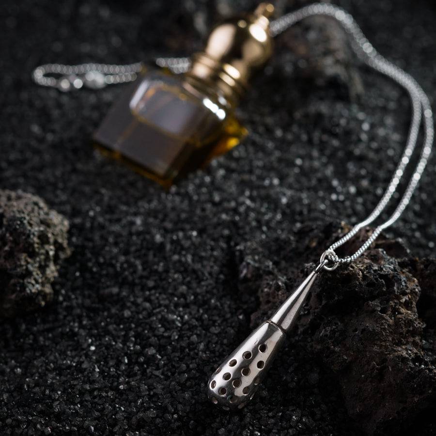 a necklace with a bottle of oil on a rock