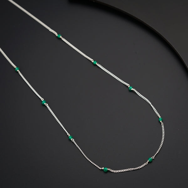 a silver necklace with green beads on a black surface