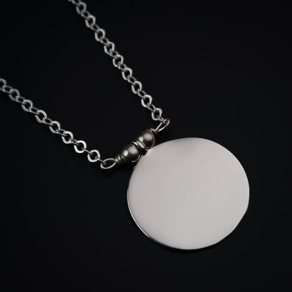 a silver necklace with a white disc on a chain