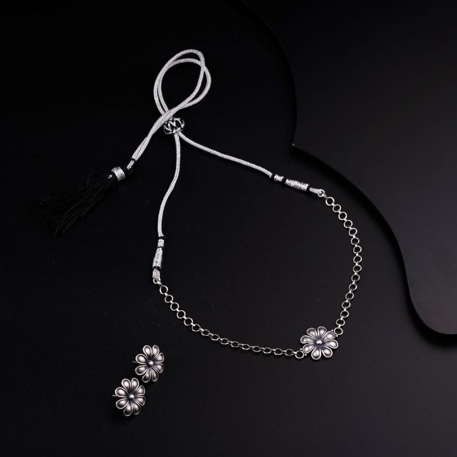 a necklace with a flower and a tassel on a black background