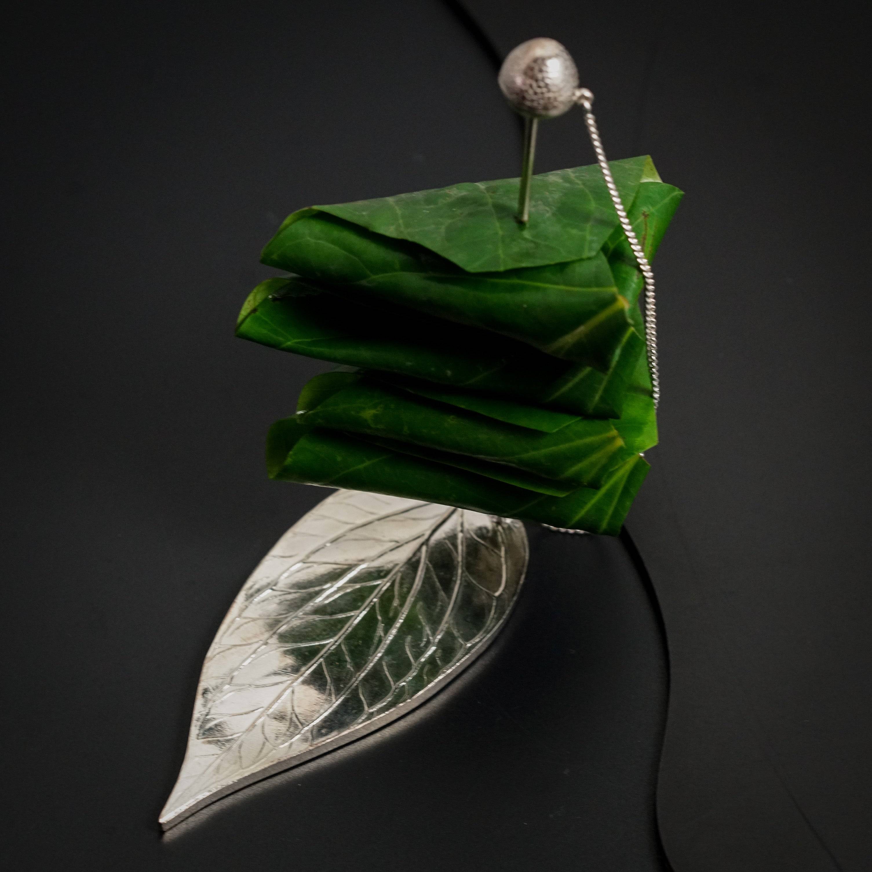 a green leaf with a silver bead hanging from it